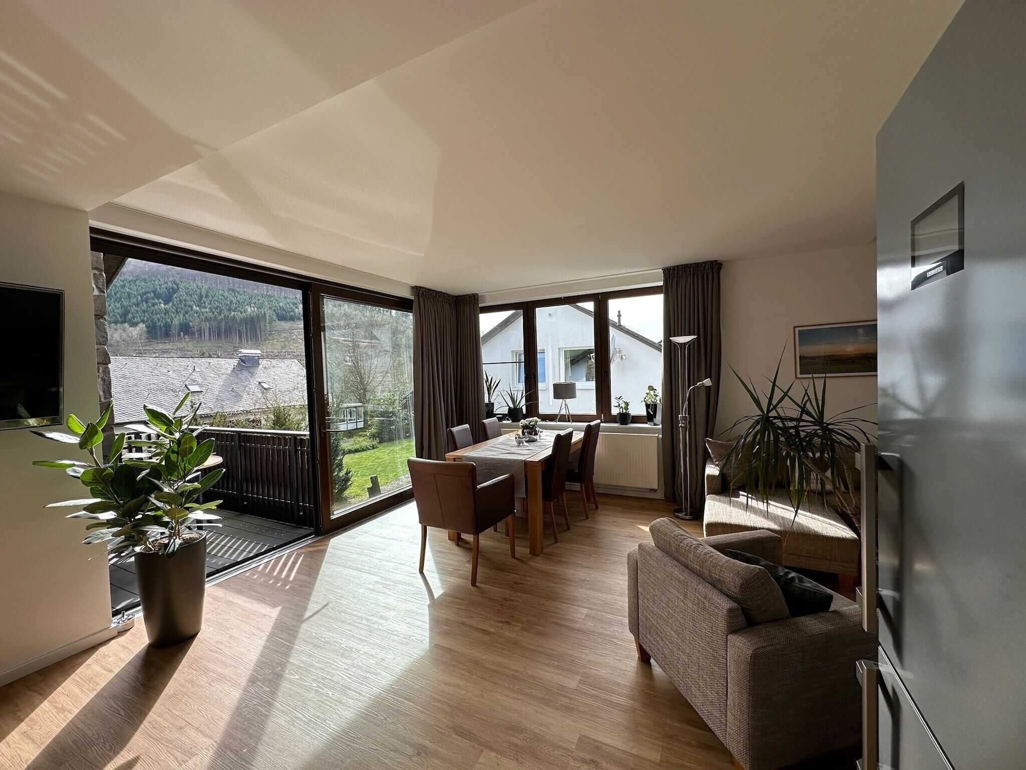 Ein großzügiger Wohnbereich mit Esstisch, Sofa und einem großen Fenster mit Blick auf eine Wohngegend.