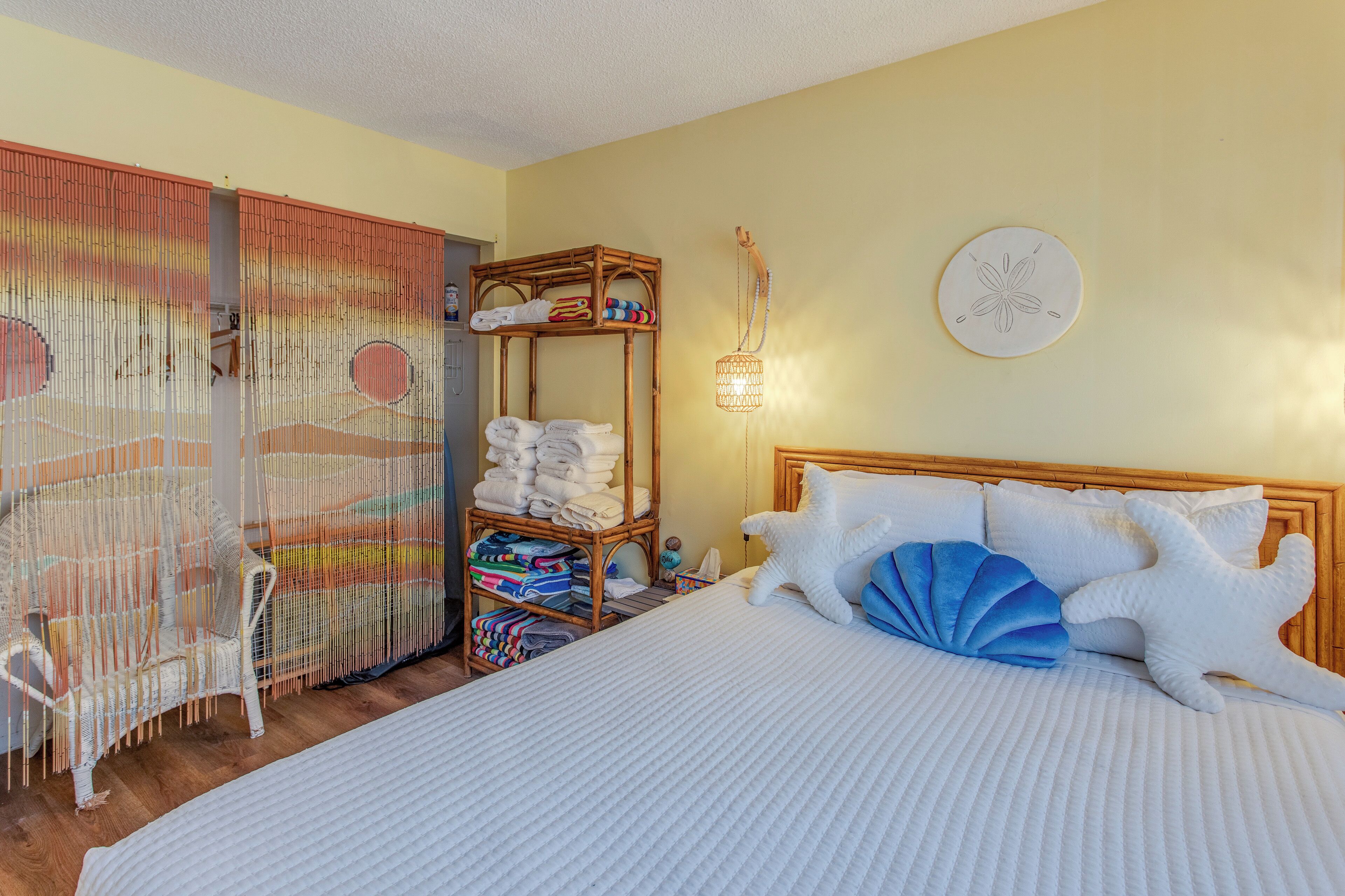 A bedroom with a bed, a wooden headboard, a wall-mounted shelf with towels, a decorative chair, and a wall art piece.