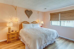 A bedroom with a large bed, wooden nightstand, bedside lamps, a heart-shaped wall decoration, and a window with blinds. - Golf, Explore & Walk to Shore! Myrtle Beach Unit (Myrtle Beach)