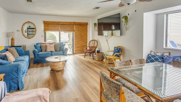Un salón amplio con piso de madera, sofás azules, una mesa de centro de vidrio y un ventilador de techo.