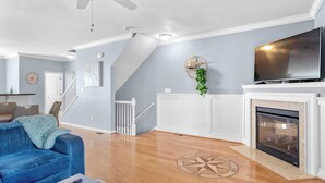 A spacious living room with a blue sofa, a fireplace, a TV, and a staircase. - Rehoboth Crossing 1 - For 10 (Rehoboth Beach)