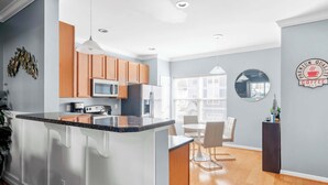A modern kitchen with wooden cabinets, a central island, and a dining area with a round table and chairs. - Rehoboth Crossing 1 - For 10 (Rehoboth Beach)