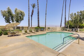 A swimming pool with lounge chairs and an umbrella, surrounded by palm trees and a fence. - Stay on the Greens! Resort-style Palm Desert Condo (Palm Desert)