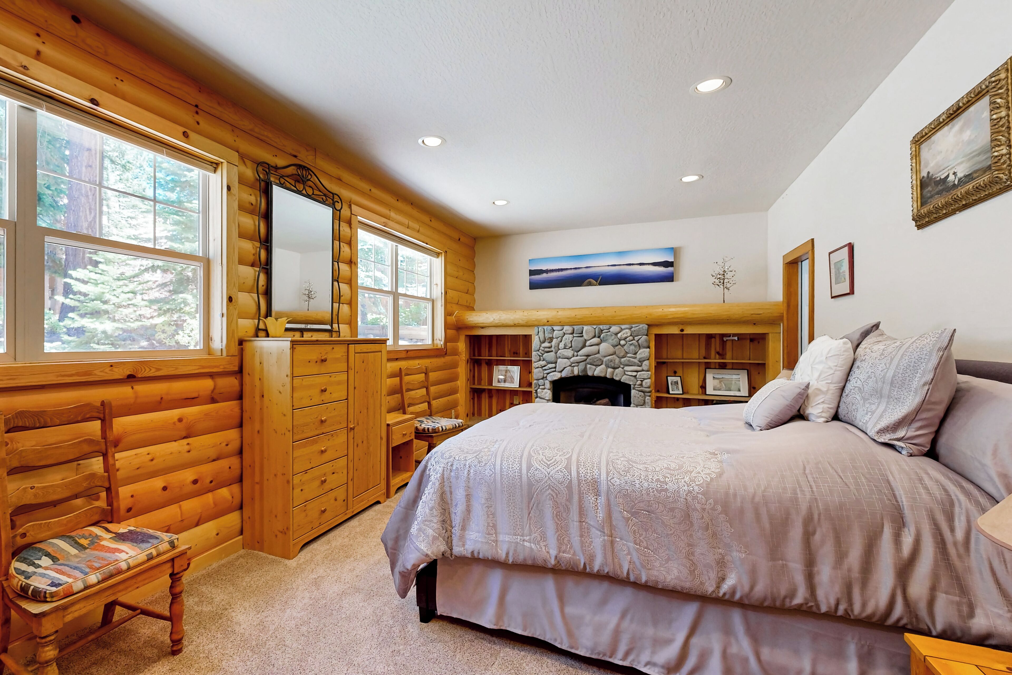 Une chambre située dans un chalet en rondins, avec un grand lit, des meubles en bois, une cheminée en pierre et une vue sur la forêt grâce à de grandes fenêtres.