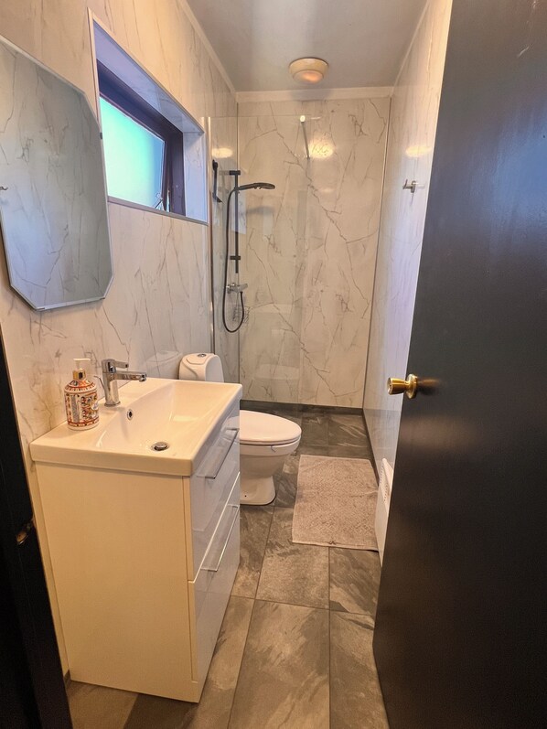 A bathroom with a white sink, toilet, and shower. - Hlíðarból Guesthouse (Hvolsvöllur)
