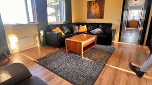 Una sala de estar moderna con un sofá de cuero negro, una mesa de centro de madera y una alfombra estampada.