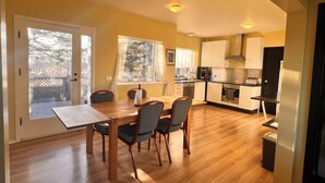 Una cocina compacta con armarios de madera, un comedor con mesa y sillas, y un ventanal corredero que da a una terraza exterior.