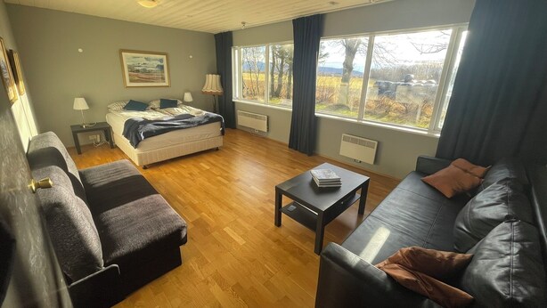 Una sala de estar moderna con una cama, un sofá, una mesita de centro y un ventanal con vistas a árboles y montañas.