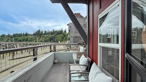 Un balcon doté de meubles en osier et d’une table en verre, offrant une vue sur un pont et une zone boisée.