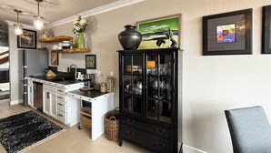 A modern kitchen with white cabinets, a black cabinet with glass doors, and a dining area with a chair. - Studio Overlooking Saratoga Passage & Cascade Mtns (Langley)