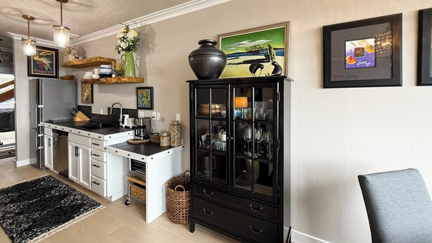 Une cuisine moderne avec des meubles blancs, un meuble noir doté de portes en verre et un coin repas avec une chaise.