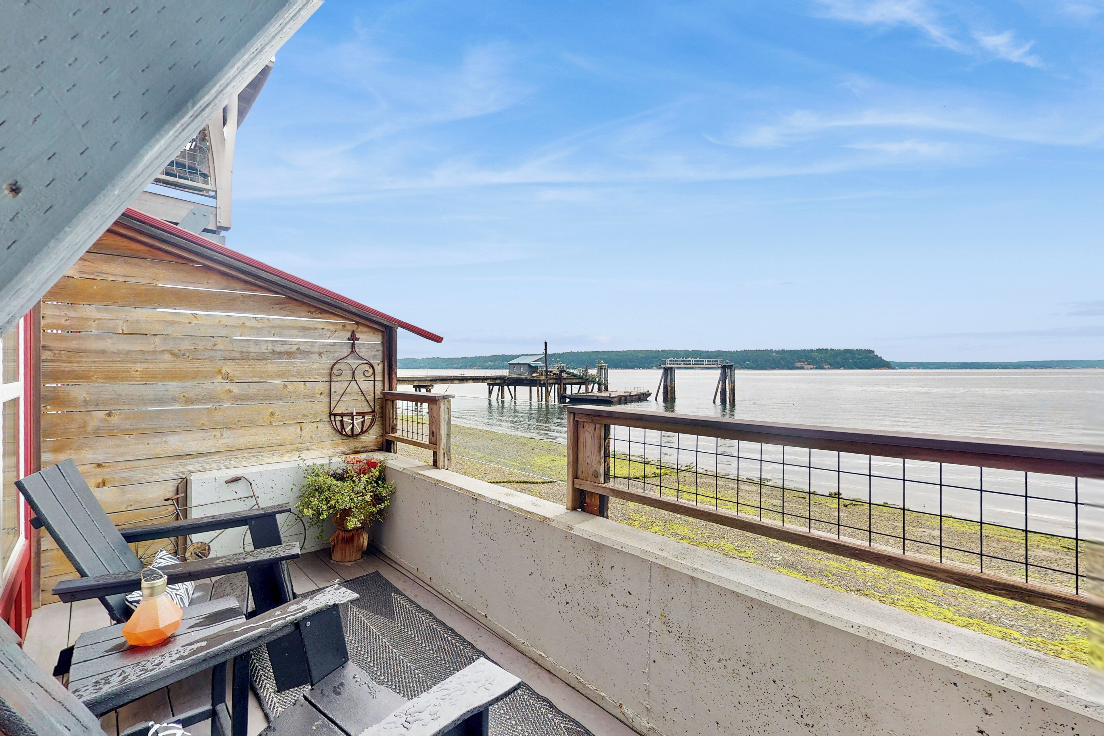 Ein Balkon mit Blick auf einen See und eine Anlegestelle, Holzmöbel und ein Blumentopf.
