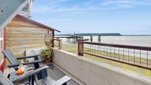 A balcony with a view of a lake and dock, wooden furniture, and a potted plant. - Studio Overlooking Saratoga Passage & Cascade Mtns (Langley)