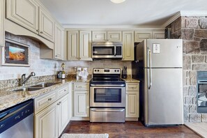 A kitchen with light-colored cabinets, a stainless steel microwave, oven, and refrigerator, a dishwasher, and a stone accent wall. - Pool + Riverfront! Couples Retreat in Smoky Mtns (Townsend)