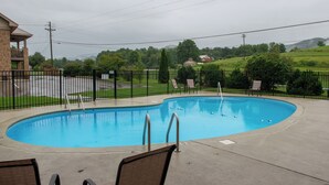 A swimming pool with a curved edge, surrounded by a black metal fence. There are lounge chairs and a concrete deck area. - Pool + Riverfront! Couples Retreat in Smoky Mtns (Townsend)