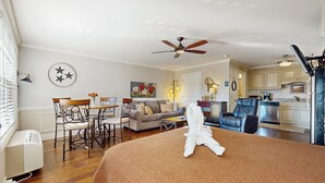 A well-lit living room with a ceiling fan, a dining area with chairs and a table, a kitchen with cabinets and a refrigerator, and a bedroom with a bed and a towel on it. - Pool + Riverfront! Couples Retreat in Smoky Mtns (Townsend)