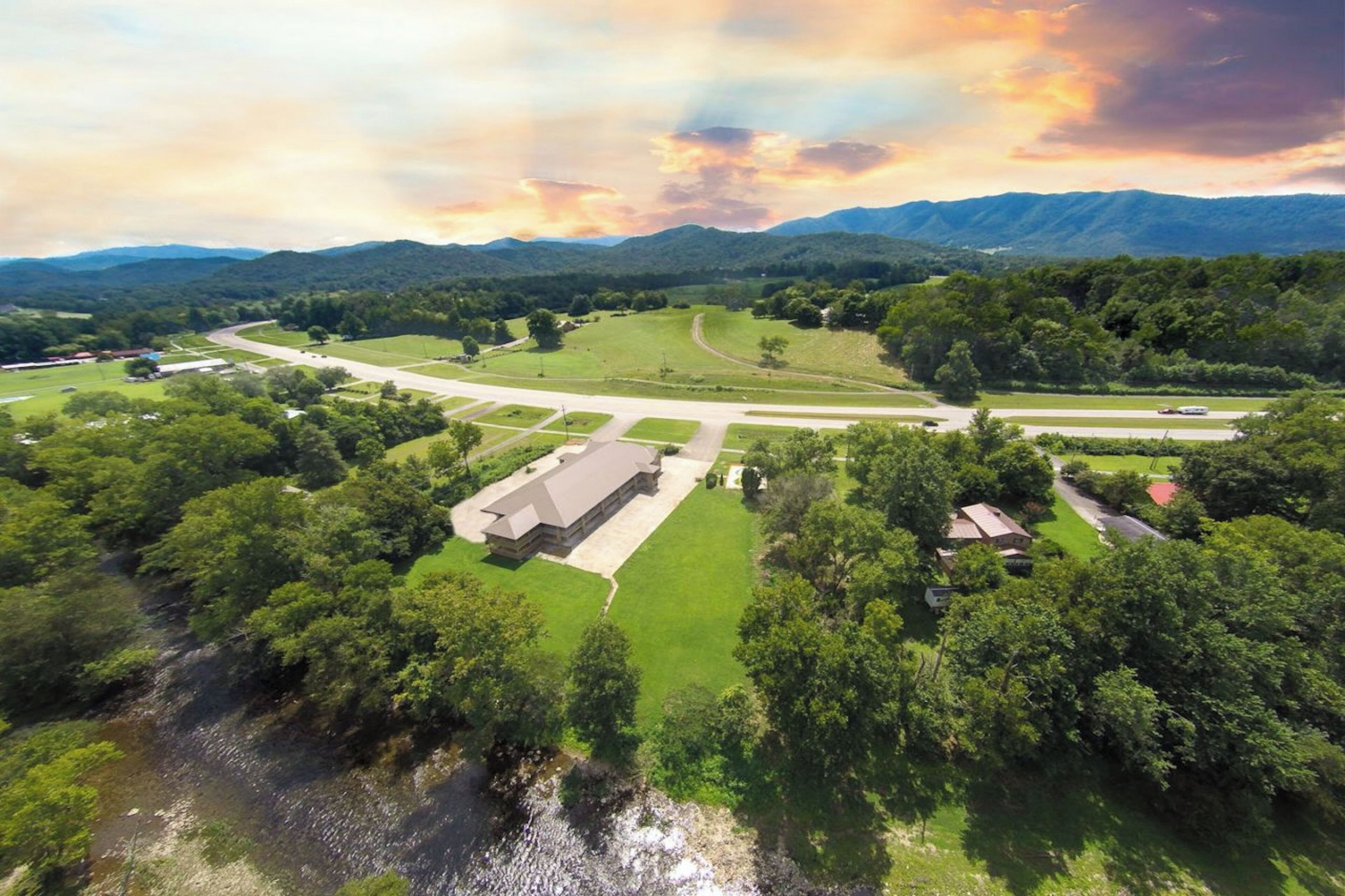An aerial view of a property with a large building, green fields, and a winding road.