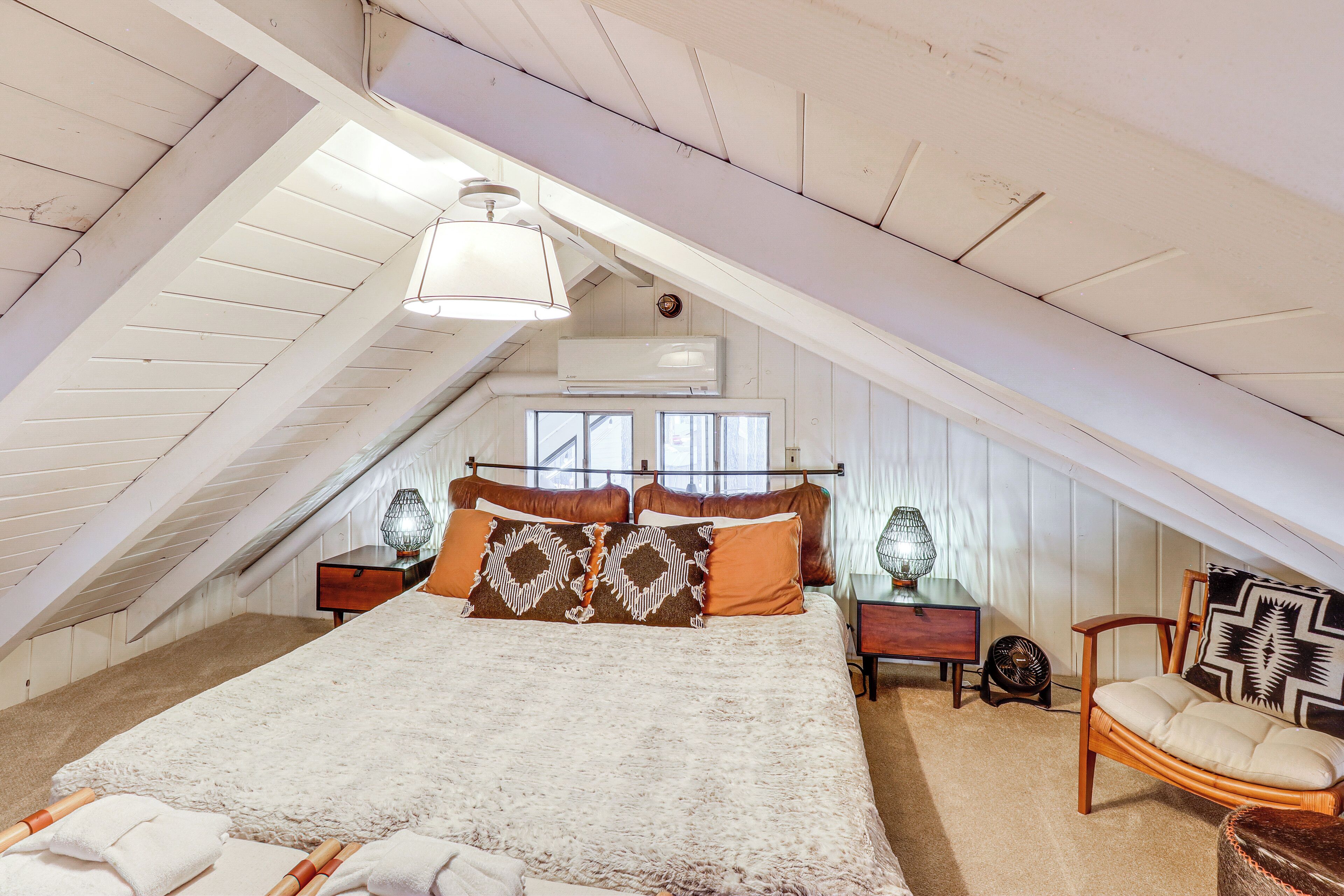 A bedroom with a sloped ceiling, a bed with patterned pillows, a chair, and bedside tables with lamps.