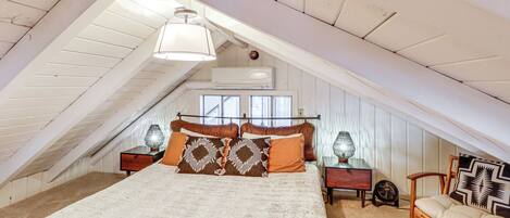 A bedroom with a sloped ceiling, a bed with patterned pillows, a chair, and bedside tables with lamps.