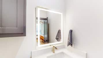 A bathroom with a white sink, a mirror with a lighted frame, and a towel hanging on the wall.