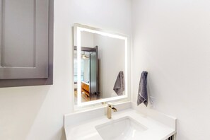 A bathroom with a white sink, a mirror with a lighted frame, and a towel hanging on the wall. - 'mckinney Marvel' Studio in Historic District (McKinney)