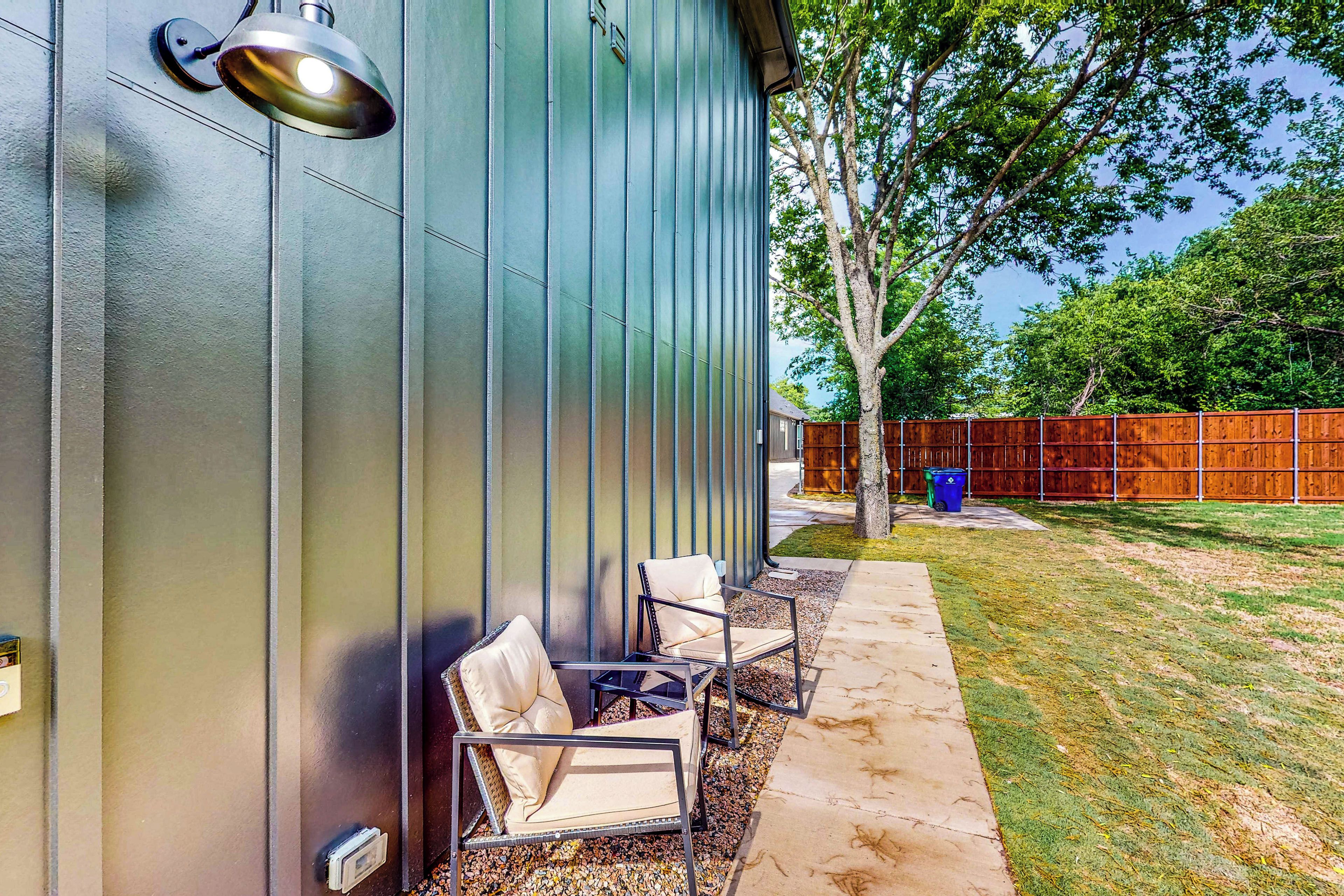 A modern building exterior with a metal siding wall, a metal lamp, and outdoor seating with chairs and a table.