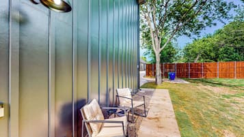 A modern building exterior with a metal siding wall, a metal lamp, and outdoor seating with chairs and a table.
