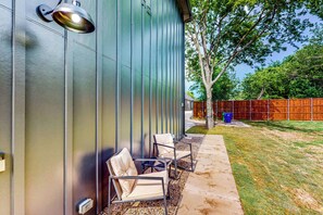 A modern building exterior with a metal siding wall, a metal lamp, and outdoor seating with chairs and a table. - 'mckinney Marvel' Studio in Historic District (McKinney)