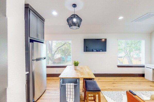 A modern kitchen with a built-in refrigerator, wooden dining table, and a hanging pendant light.