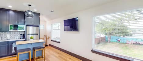 A modern kitchen with dark cabinets, a wooden countertop, and a large window with blinds.