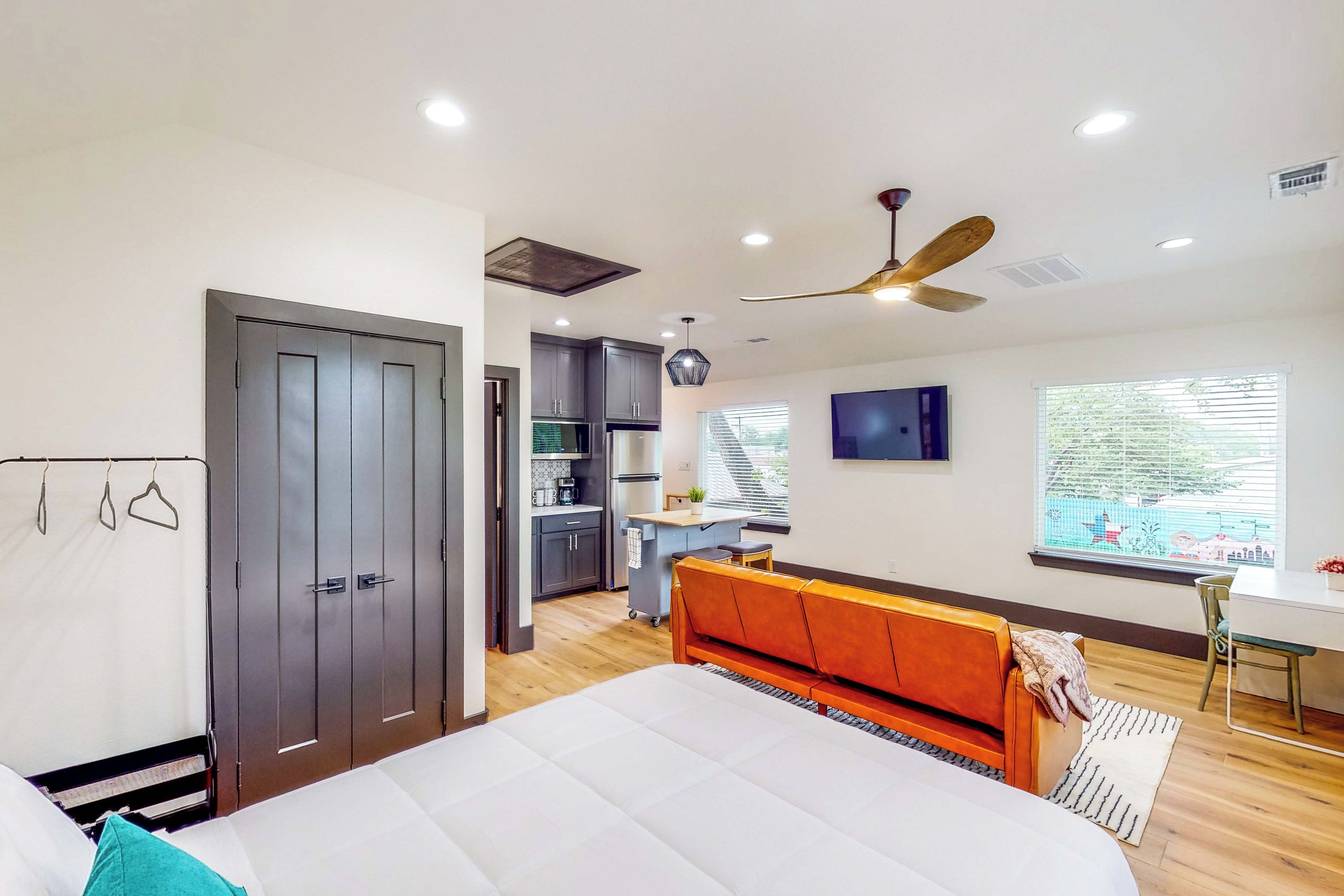 A bedroom with a bed, a desk, a chair, a wardrobe, and a kitchenette.