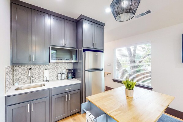 A modern kitchen with grey cabinets, a stainless steel refrigerator, a microwave, and a wooden dining table with a potted plant.