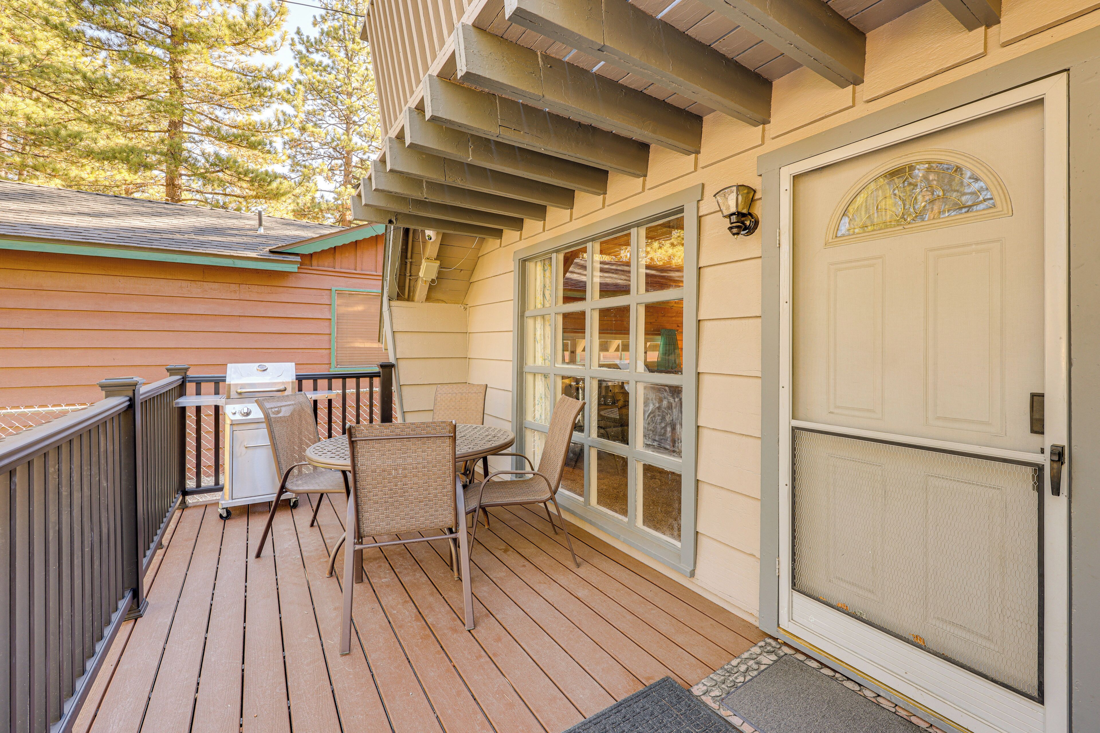 A wooden deck with a grill, outdoor furniture, and a screened door.