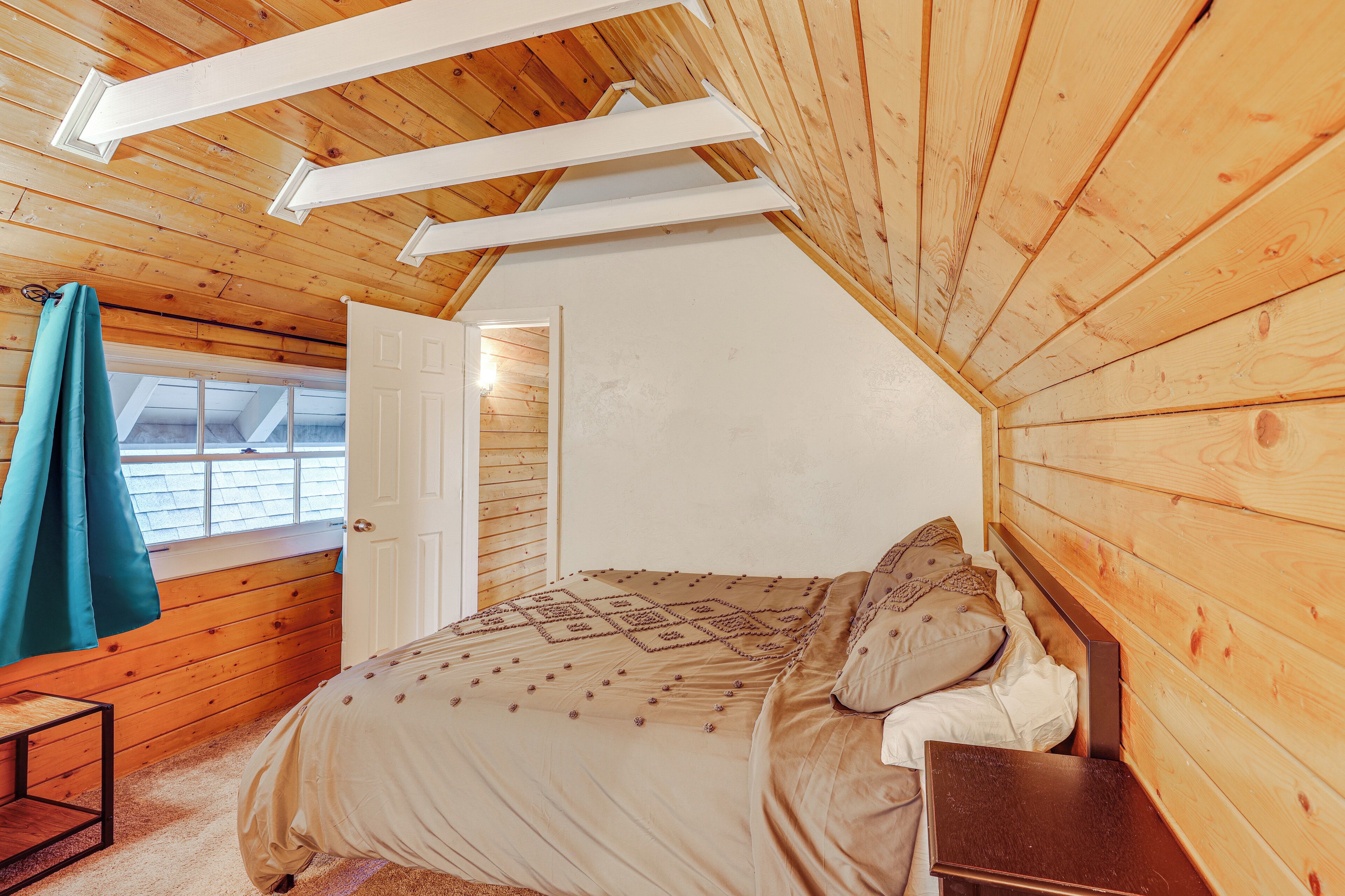 A bedroom with a sloped ceiling, wooden walls, a bed with a patterned bedspread, and a window with a view of the outside.
