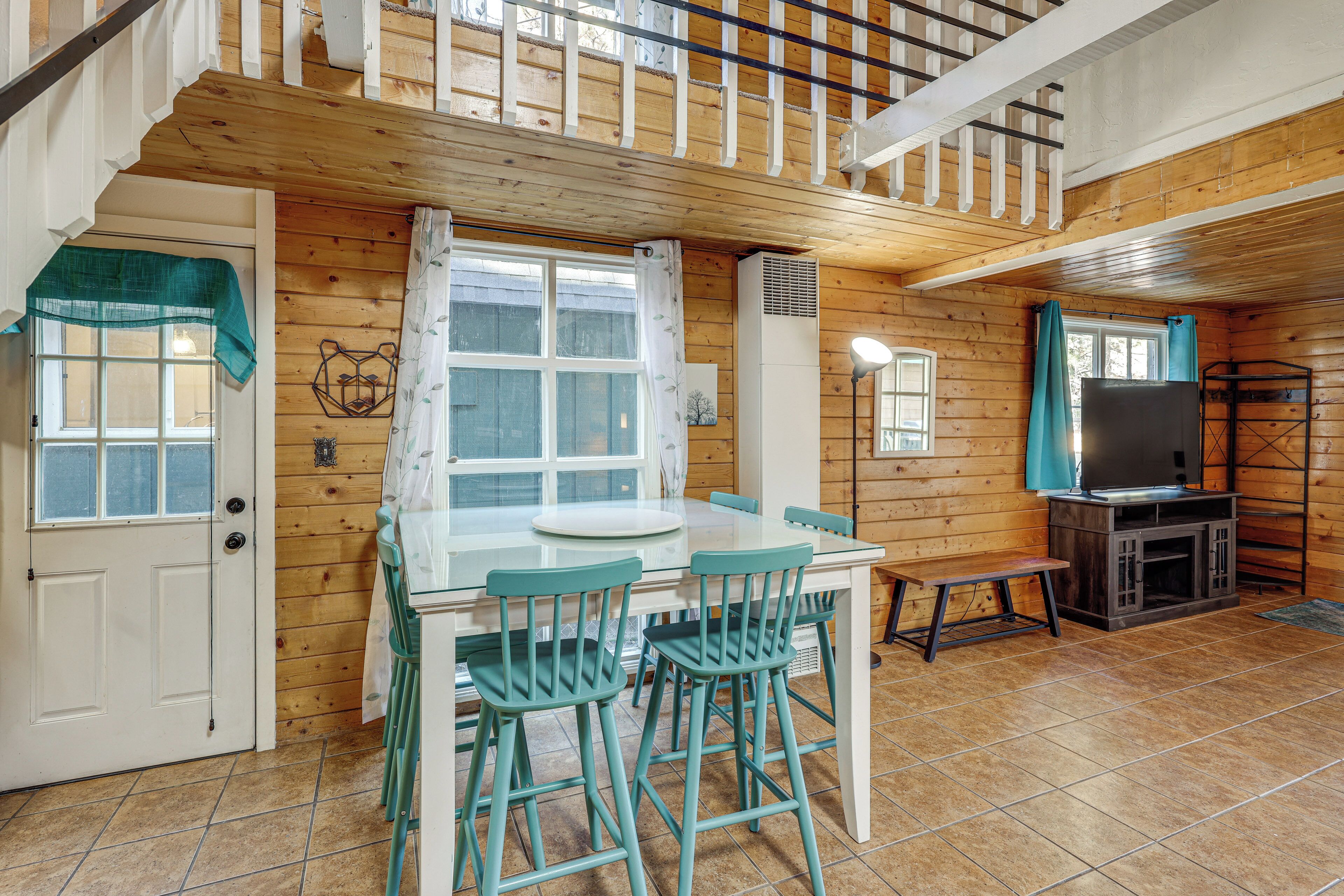 A wooden interior with a dining table, chairs, a bench, a television, and a staircase.