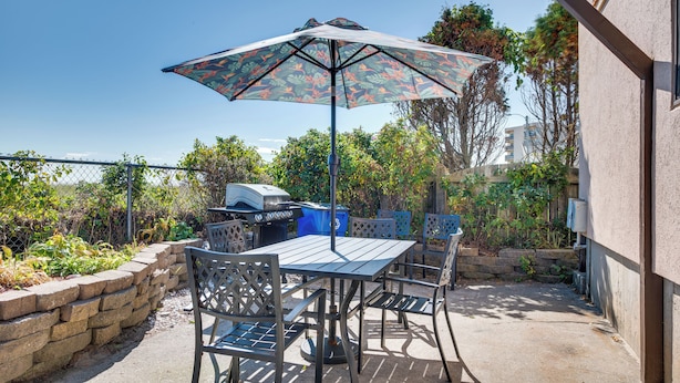 Un patio al aire libre con mesa y sillas, una parrilla y un parasol estampado.