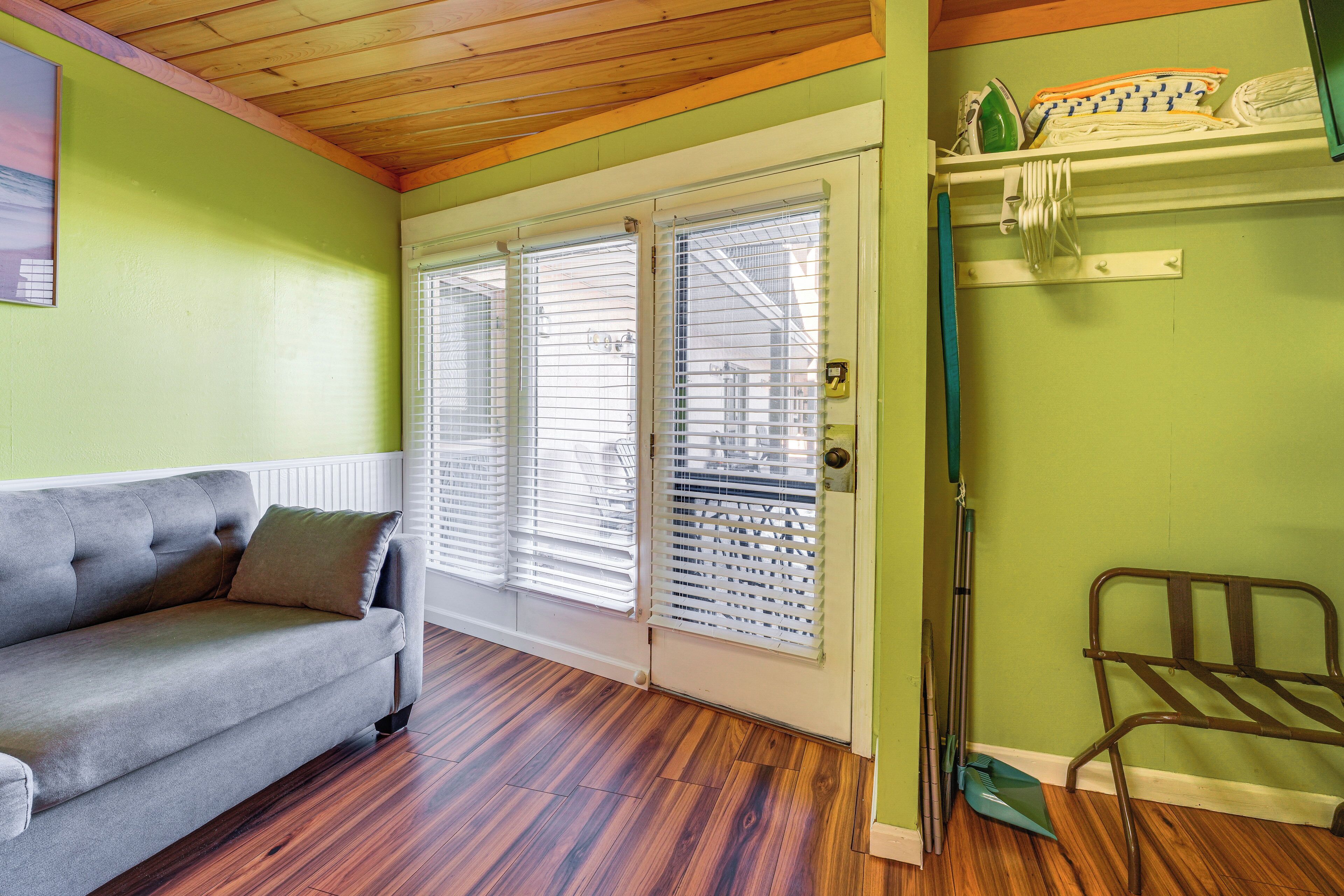 A room with a grey sofa, wooden flooring, a door with white blinds, and a metal chair.