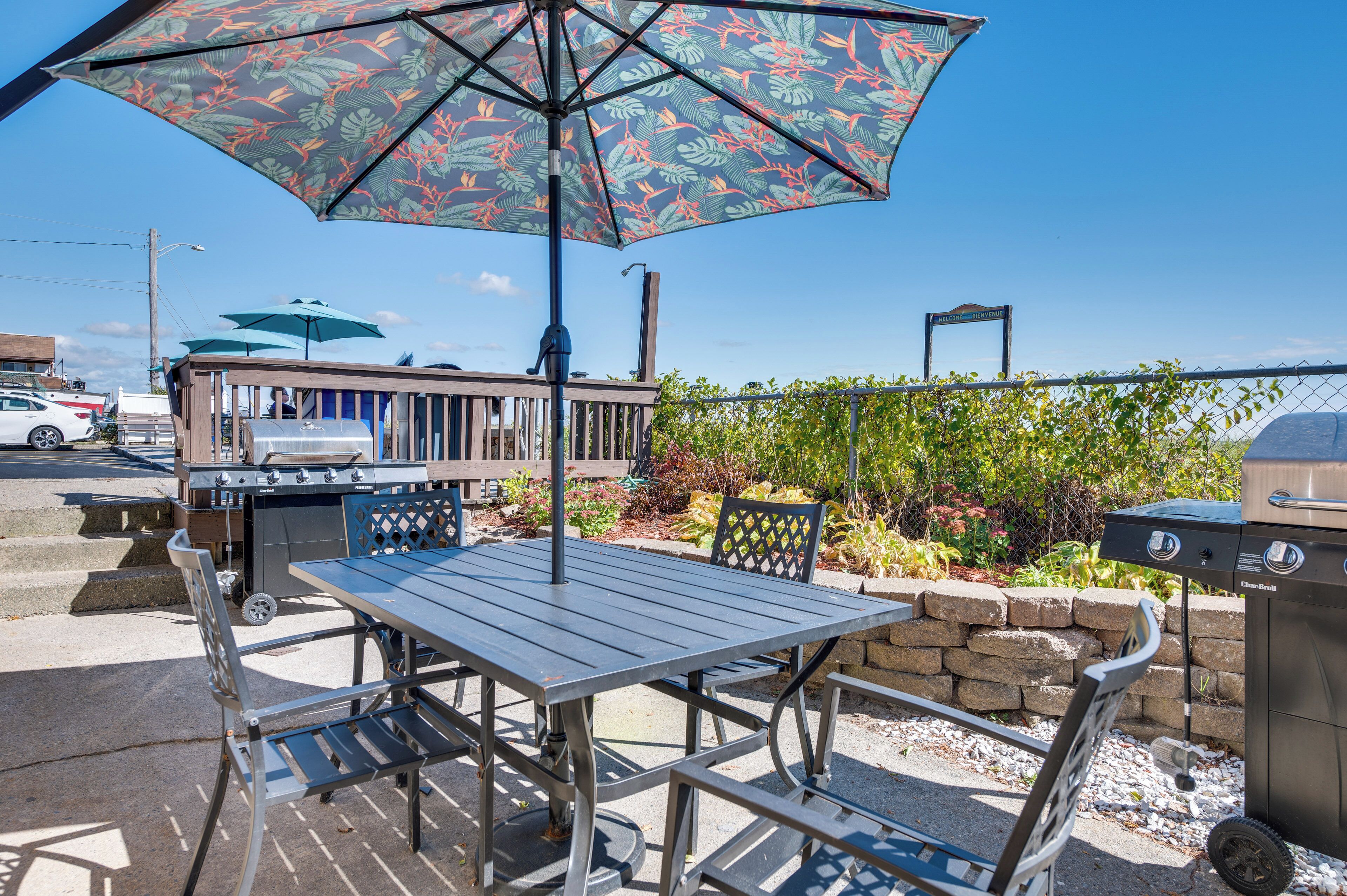 Un patio al aire libre con una mesa, sillas, una parrilla y un parasol decorativo.