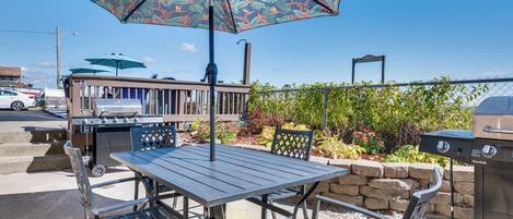 Un patio al aire libre con una mesa, sillas, una parrilla y un parasol decorativo.