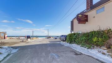 A coastal road with a building on the right, a sign reading "The Shell & Sand", and parked cars.