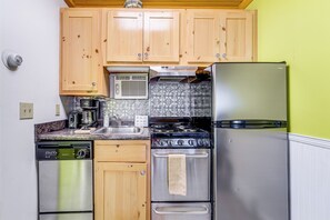 Una cocina compacta con armarios de madera, lavavajillas de acero inoxidable, estufa y refrigerador.
