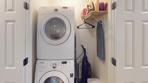 A laundry room with two stacked washing machines, a drying rack, and a shelf with cleaning supplies. - Steps to Riverfront: Dtwn Bluffton Studio! (Bluffton)