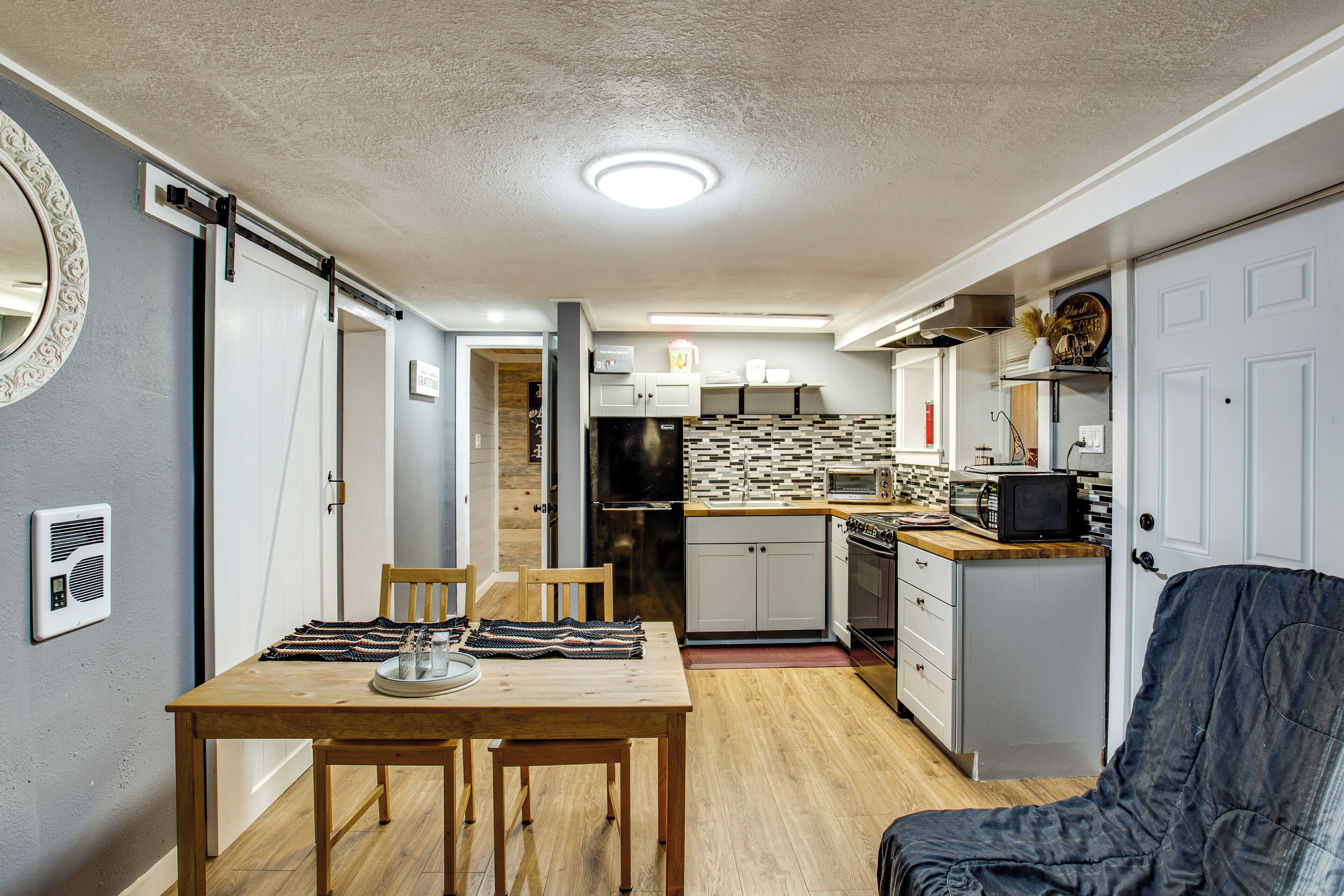A compact kitchen with a microwave, toaster, and refrigerator. There is a dining table with chairs and a small seating area with a couch.