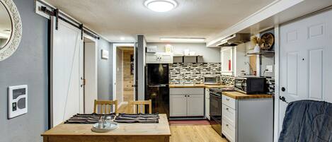 A compact kitchen with a microwave, toaster, and refrigerator. There is a dining table with chairs and a small seating area with a couch.