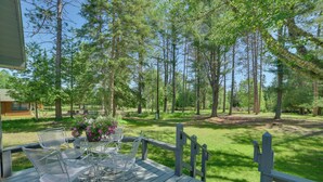 Une terrasse en bois, agrémentée de mobilier d’extérieur, entourée d’une pelouse et de grands arbres.