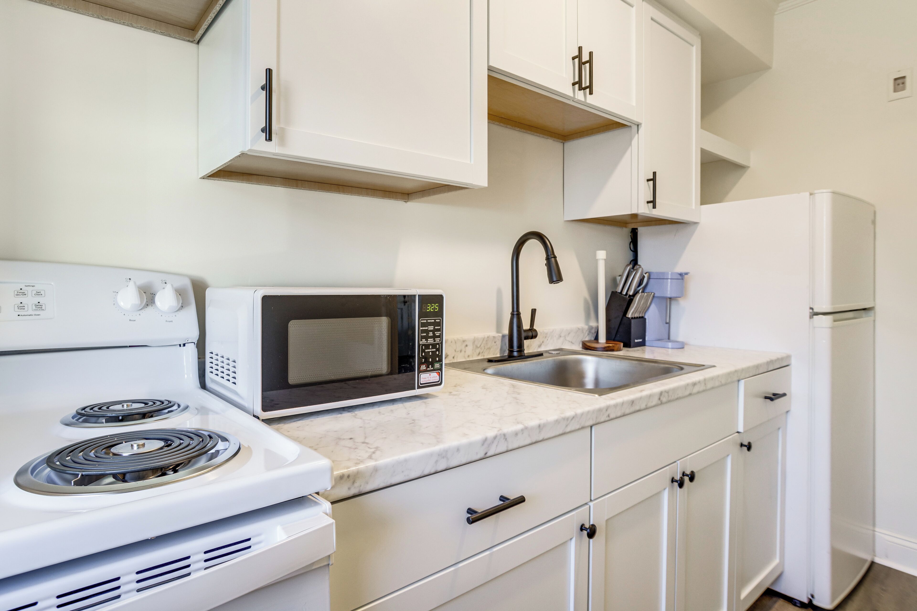 A kitchen with white cabinets, a microwave, a stove, a sink, and a refrigerator.