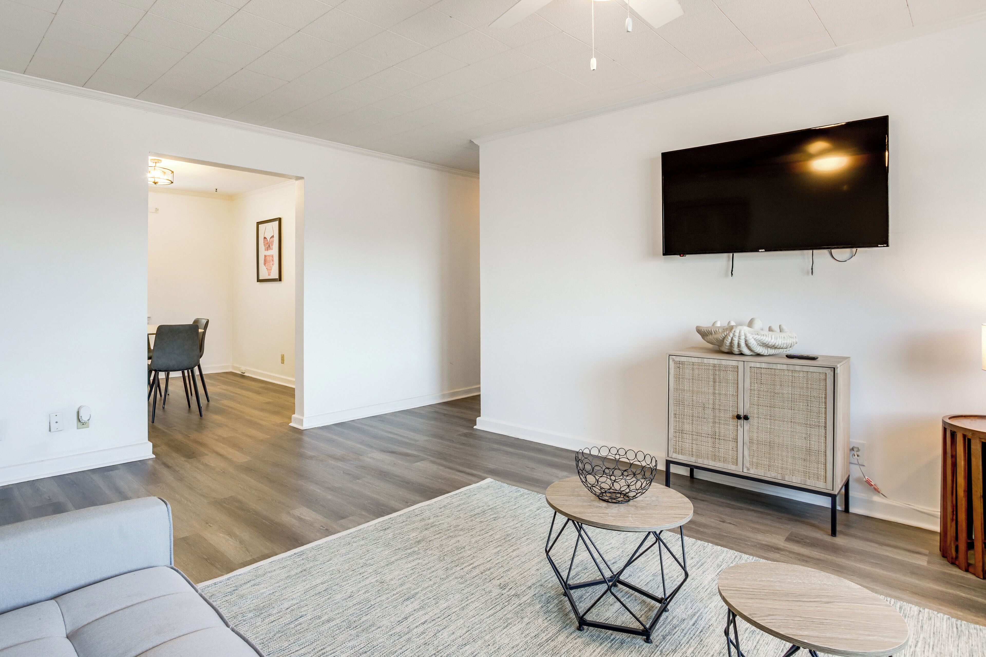 A modern living room with a flat-screen TV, a grey sofa, a wicker cabinet, and a round coffee table.