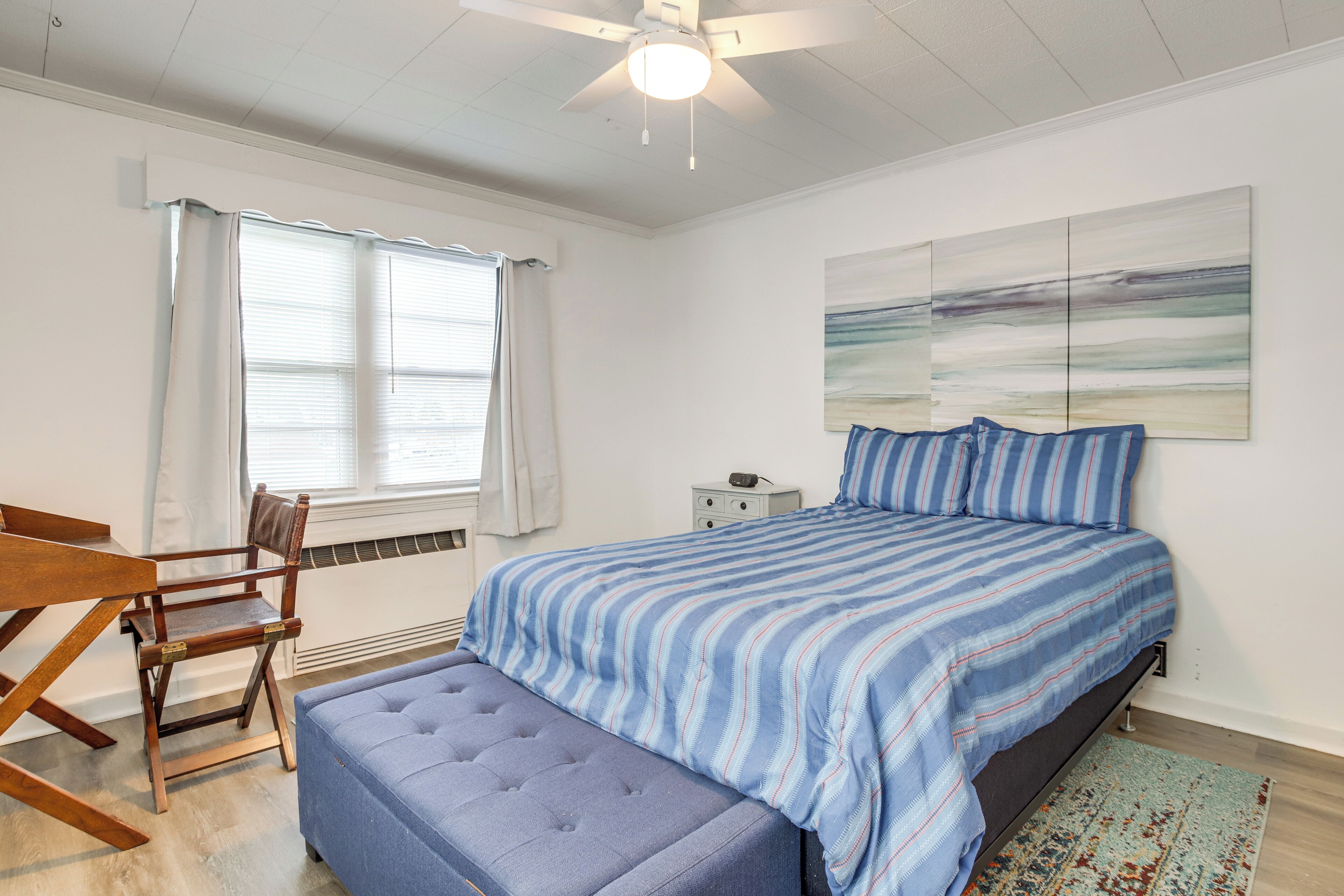 A bedroom with a bed, a chair, a bench, a ceiling fan, and a window with curtains.