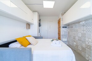 A bedroom with a bed, pillows, a bedside table, a wardrobe, and a patterned wall. - WELCS STUDIO 307 EMP with sea views (Empuriabrava)
