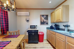 Una cocina compacta con armarios de madera, un microondas, un cesto de basura y una mesa de comedor con individuales.